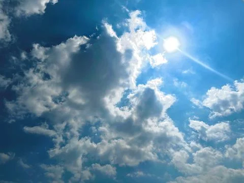 Bright Sun Shining Through Fluffy White Cumulus Clouds in Clear Blue Sky Foto stock