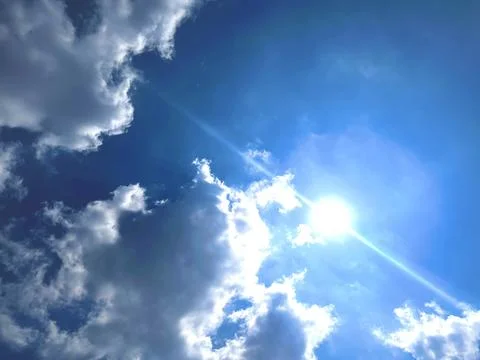 Bright Sun Shining Through Fluffy White Cumulus Clouds in Clear Blue Sky Stock-Fotos