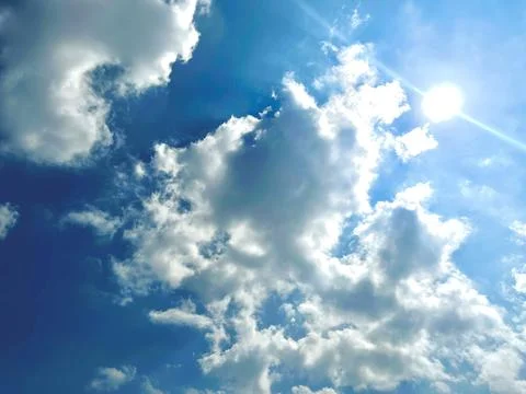 Bright Sun Shining Through Fluffy White Cumulus Clouds in Clear Blue Sky Foto stock