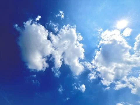 Bright Sun Shining Through Fluffy White Cumulus Clouds in Clear Blue Sky Stock-Fotos