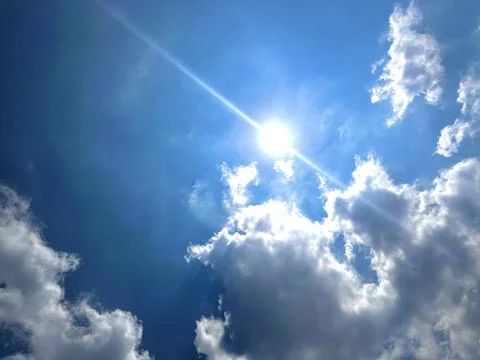 Bright Sun Shining Through Fluffy White Cumulus Clouds in Clear Blue Sky Stock-Fotos