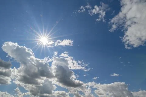 Bright sun shining through fluffy clouds on a clear blue sky brings warmth .. Stock Photos