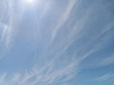 Bright sun shining through soft wispy clouds in blue sky Stock Photos