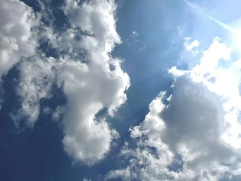 Bright Sun Shining Through White Fluffy Clouds in a Beautiful Clear Blue Sky Foto stock