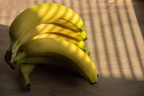Bright sun shining through window blinds and casting stripes on bananas and.. Stock Photos