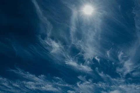 Bright sun shining through wispy clouds in a deep blue sky. Stock Photos