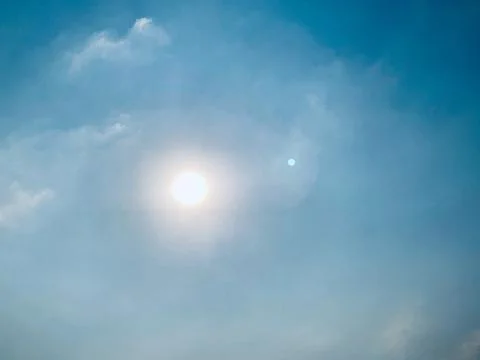 Bright Sun in Soft Blue Sky with Thin Clouds and Lens Flare Foto stock