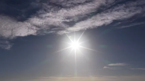 Bright sun with starburst rays shining through scattered clouds in blue sky Stock Footage 338013529