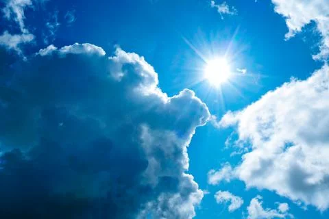 Bright sun in thick blue clouds against a blue sky. Stock Photos