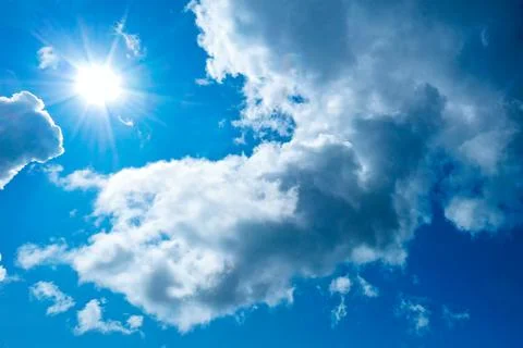 Bright sun in thick blue clouds against a blue sky. Stock Photos