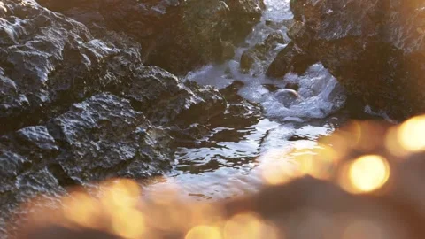 Bright sunlight illuminates water flowing between dark coastal rock formations. Stock Footage 337412203