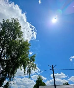Bright Sunlight Shines Through Clouds in a Clear Blue Sky Over Trees Stock Photos