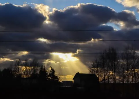Bright sunlight through dark clouds illuminates a house in the village. Stock Photos