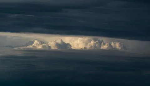 Bright sunlit cloud visible through opening in dark cloud Stock Photos