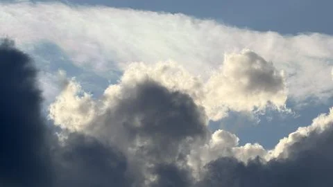 Bright sunlit cumulus cloud breaking through heavy, dark rain clouds Stock Photos