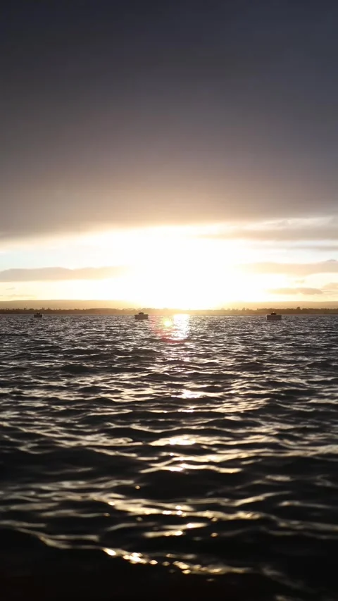 Bright sunset reflecting on dark shimmering waves with distant calm boats Stock Footage 327924440