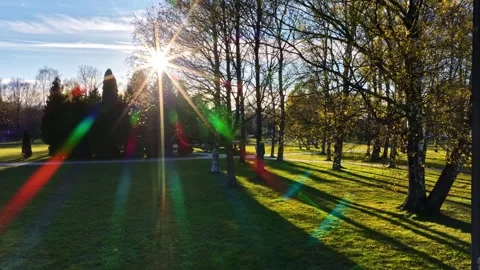Bright sunshine with lens flare casting long shadows across a green park in Stockbeeldmateriaal 336724977