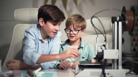 At a bright table, two schoolchildren watch a 3D printer work and play with it Stock Footage 335375311