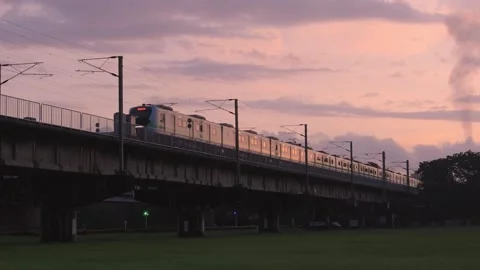 A bright train passes over a viaduct on green grass at sunset. Stock Footage 278179643