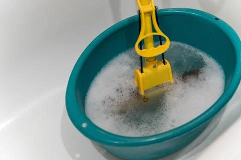 Bright turquoise basin filled with soapy water, featuring a yellow cleaning tool Stock Photos