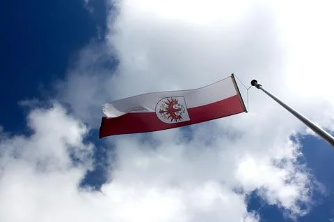 Bright Tyrolian flag waving against a blue sky with clouds Stock Photos