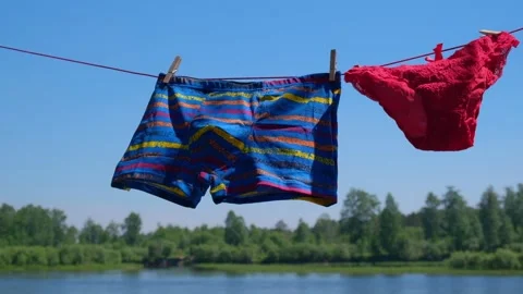 Bright underwear is drying on rope by river, swaying in wind. slow motion. Stock Footage 231616945
