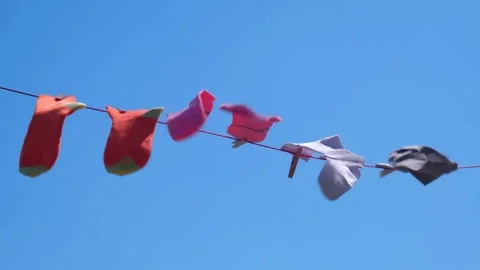 Bright unisex socks are drying on rope with clothespins against sky background. Stock Footage 199084038