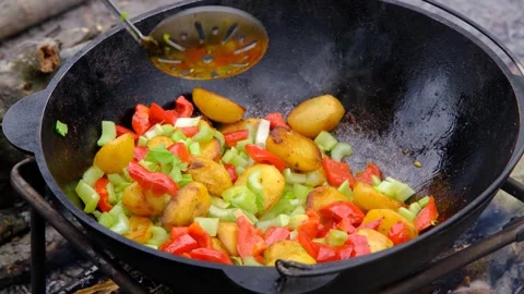 Bright vegetables are fried in a cauldron over an open fire. Vegetables are Stock Footage 280354971