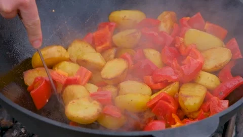 Bright vegetables are fried in a cauldron over an open fire. Vegetables are Stock Footage 316391677