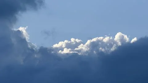 Bright white cumulus clouds emerging from behind a massive dark storm cloud Stock Photos