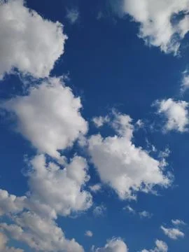 Bright white cumulus clouds scattered across a clear blue sky on a sunny day. Stock Photos