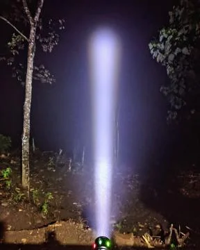 A bright white light beam shining upwards from a small flashlight Stock Photos