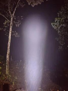 A bright white light beam shining upwards from a small flashlight Stock Photos