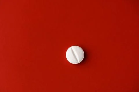 Bright white pill resting on a bold red surface, showcasing its smooth text.. Foto stock