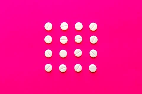 Bright white pills or tablets in a row on pink background. Stock Photos