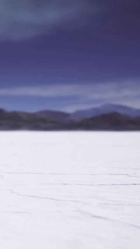 Bright white salt flat under cloudy sky with distant mountains in background Stock Footage 334183452