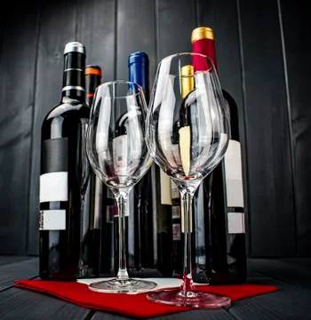 Bright wine glasses on red tablecloth, bottles of red wine on gray wooden bac Stock Photos