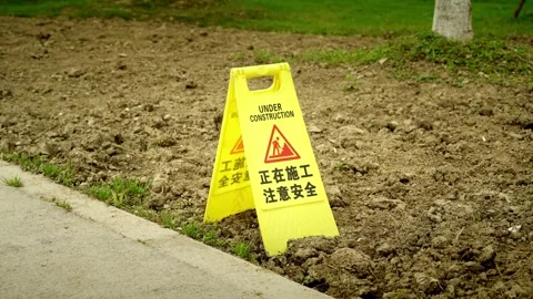 A Bright Yellow Caution Sign Standing on Tilled Soil at a Park Landscapi Stock-Footage 332855533