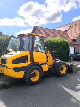 A bright yellow compact wheel loader is parked outside on a sunny day. Stock Photos