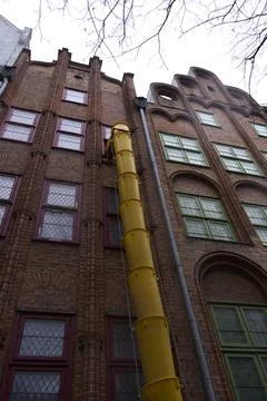Bright Yellow Construction Pipe on a Brick Building for Waste Disposal Stock Photos