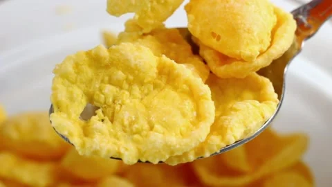 Bright yellow cornflakes for breakfast falling down the spoon close up Stock Footage 232465072