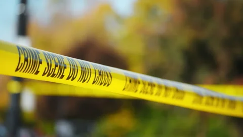 A bright yellow Crime Scene Do Not Cross tape stretched across an urban Stock Footage 297095083