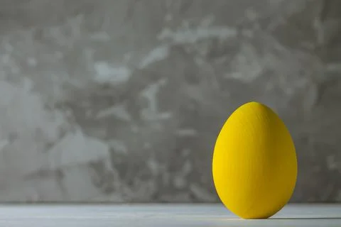 Bright yellow Easter egg, standing on white wooden surface on gray concrete b Stock Photos