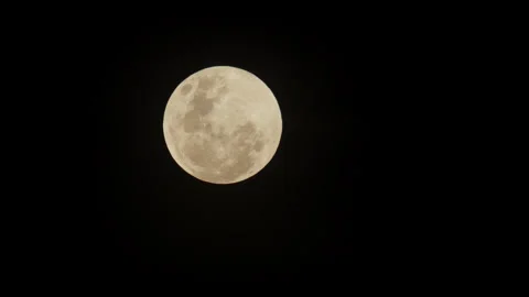 A bright yellow full moon the its visible craters, glowing against the dark Stock Footage 332780932