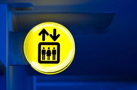 Bright yellow lift or elevator symbol, sign on blue wall background with neon Stock Photos