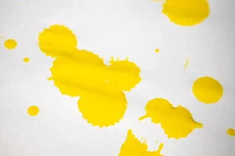 Bright yellow paint splashes of various sizes scattered on a white. Stock Photos