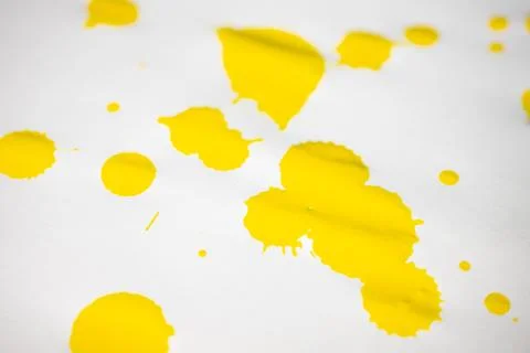 Bright yellow paint splashes of various sizes scattered on a white. Stock Photos