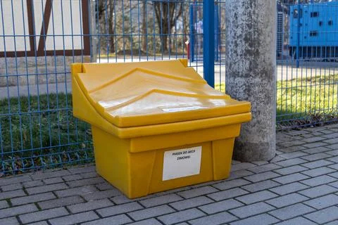 A bright yellow plastic container for road salt or grit stands on a paved Stock-Fotos