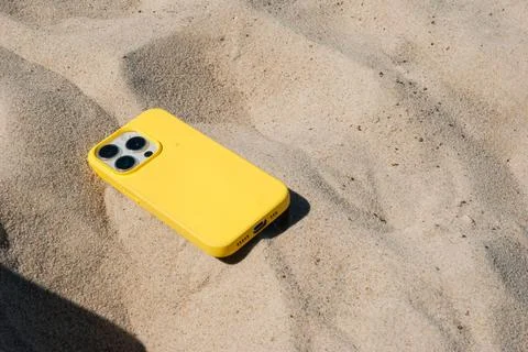 Bright yellow smartphone case on sandy beach under clear blue sky showcasing  Stock Photos