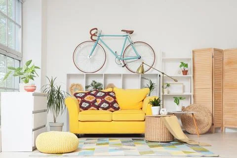 Bright yellow sofa with patterned pillows in a modern living room a bicycle m Stock Photos